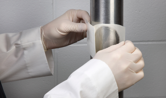 A lab technician applies a Neogen® Petrifilm® Rapid Plate on a pipe to test for environmental contamination.
