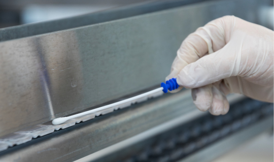 A technician uses a Neogen® Clean-Trace® ATP testing swab on a food conveyor.